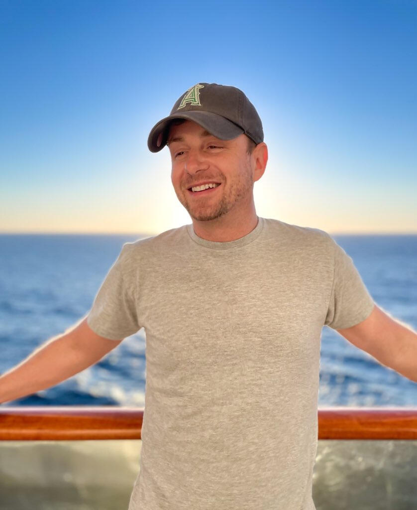 Ryan in a cap on a boat deck with the sea behind him